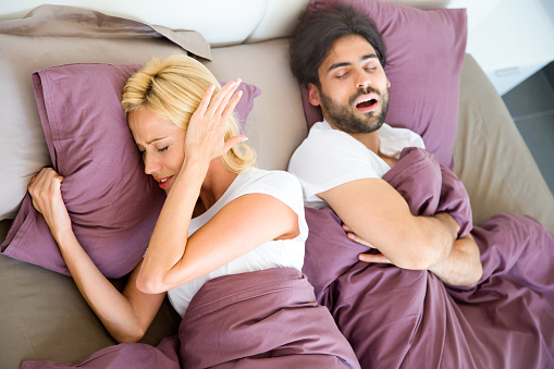 Woman covering ears while man snores in sleep.