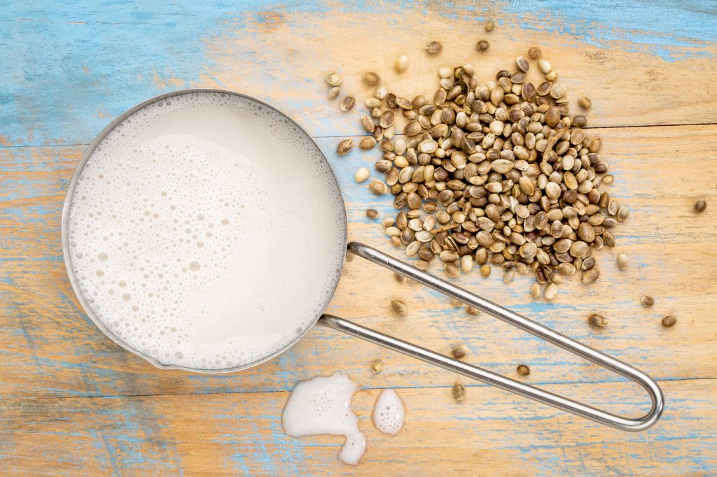 hemp milk in measuring cup with seeds against wooden background